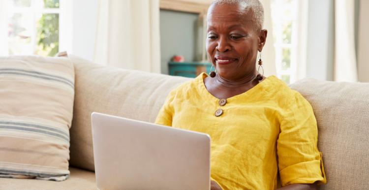 Black woman sitting on sofa smiling at laptop 
