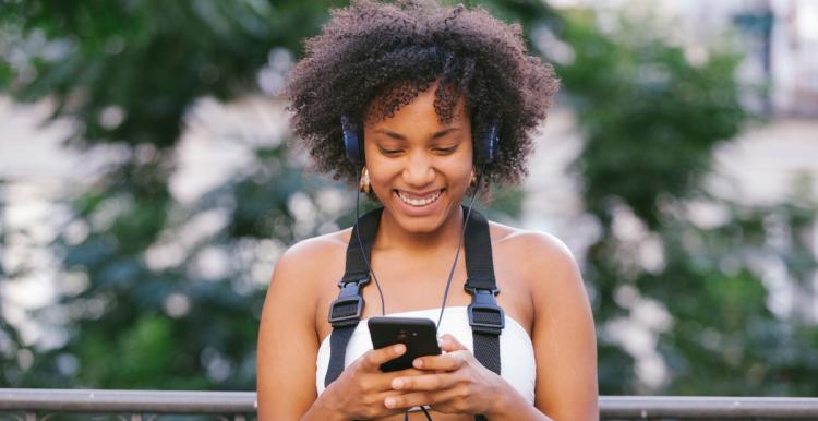 A woman listening to audiobooks woman outside holding and smiling down at her phone