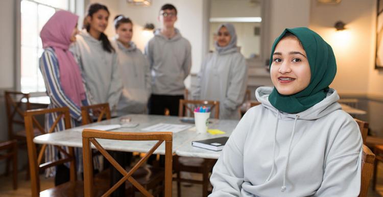 Young volunteer wearing a headscarf sitting down with a group of other young volunteers behindlunteers with one