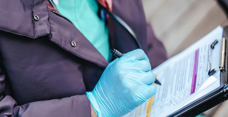 Healthcare professional in scrubs sitting down and writing on a clipboard