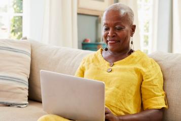 Black woman sitting on sofa smiling at laptop 