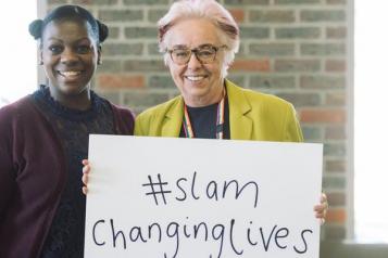 Two women smiling holding a 'SLAM Changing lives' poster