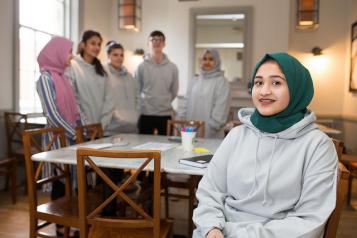 Young volunteer wearing a headscarf sitting down with a group of other young volunteers behindlunteers with one 