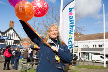 Healthwatch employee holding balloons infront of a Healthwatch sign