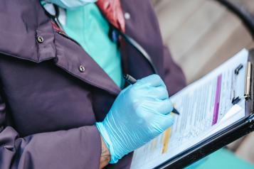 Healthcare professional in scrubs sitting down and writing on a clipboard