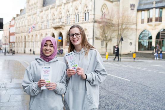 Two young female volunteers holding Healthwatch leaflets