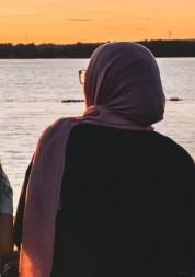 back of a lady in a hijab looking at the sunset